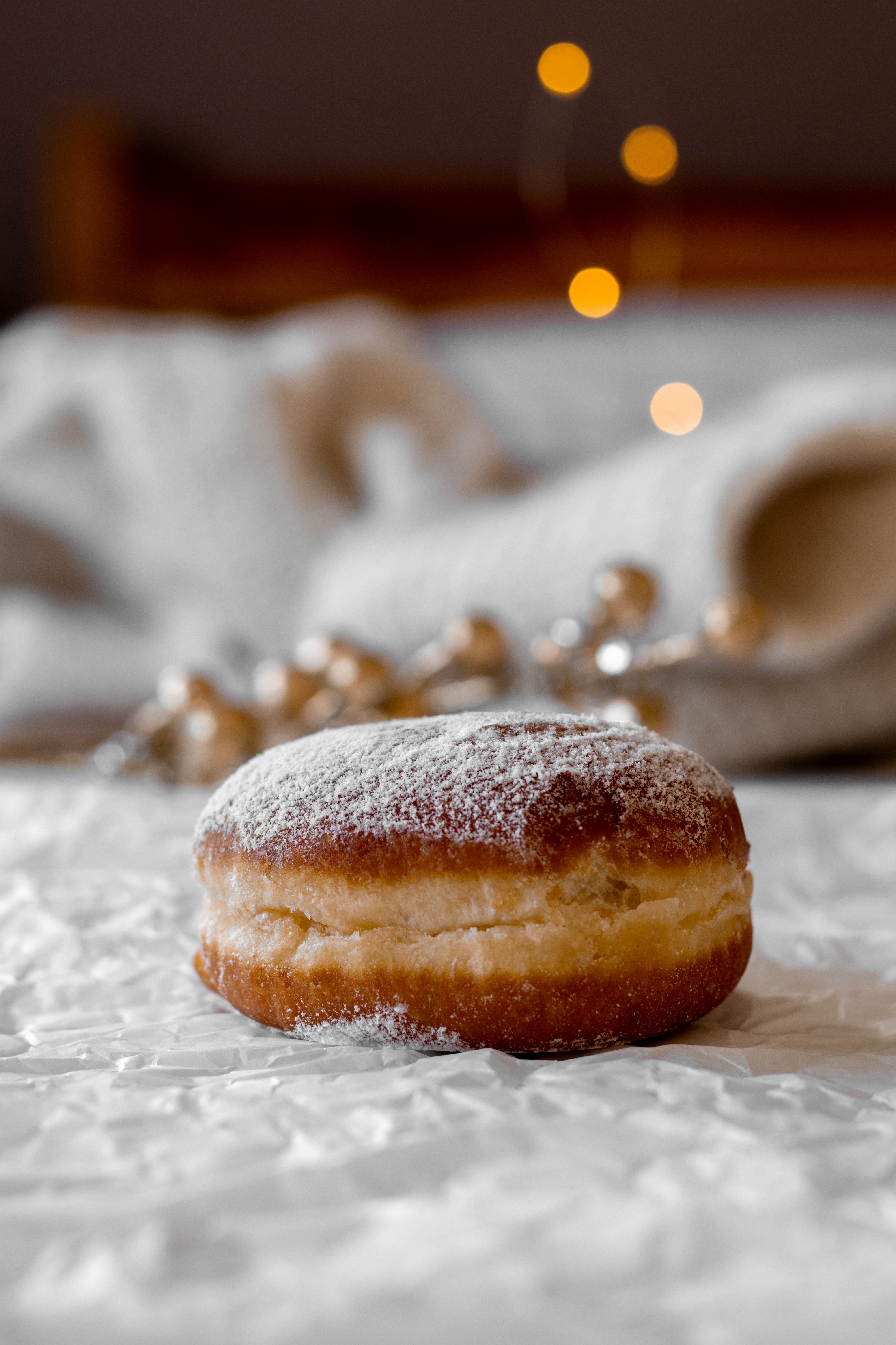 A tempting doughnut coated with sugar, resting on crumpled paper with blurred lights in the background.