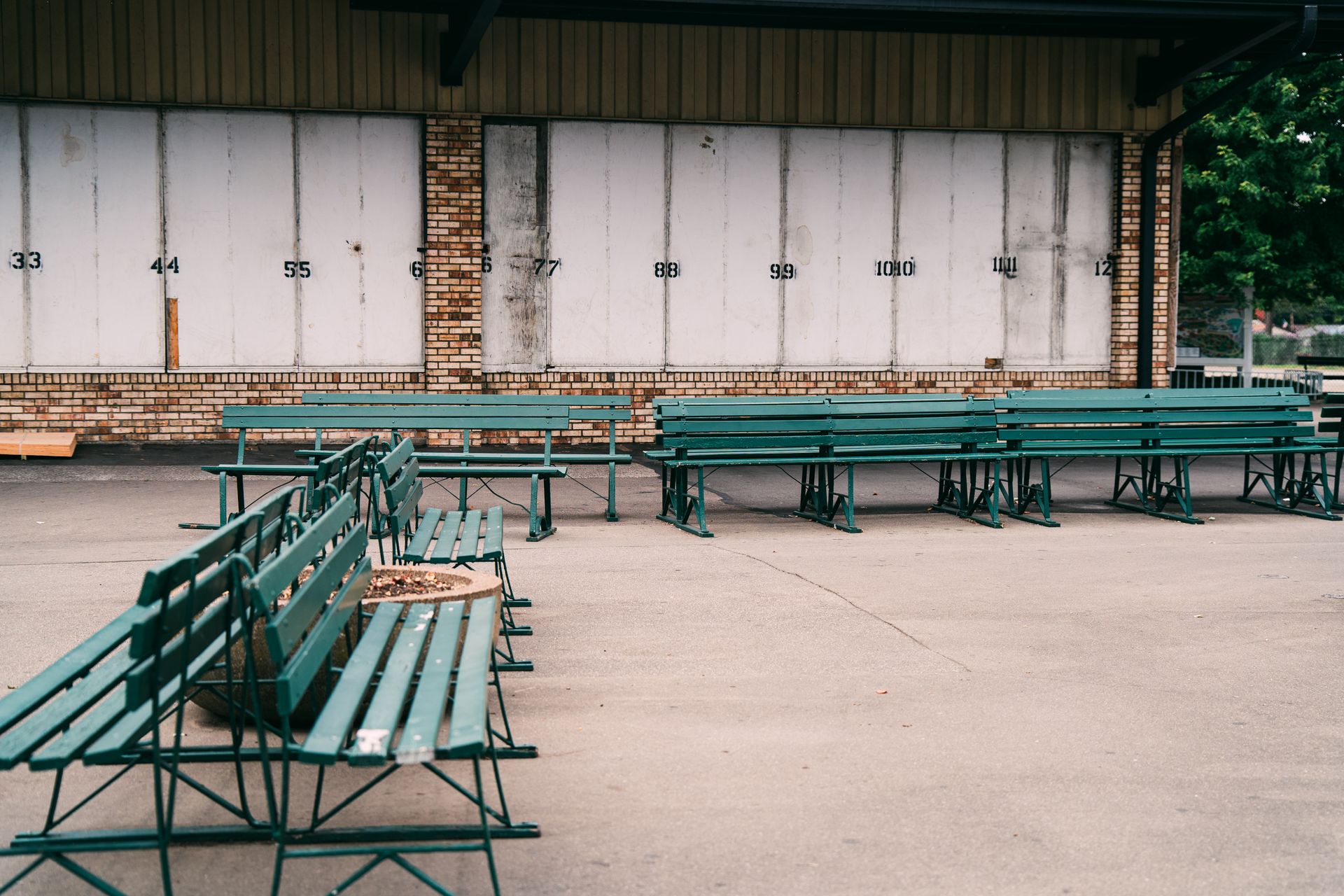 A row of green benches in a deserted urban area with numbered walls.