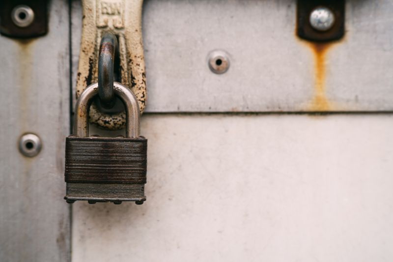 Close-up of a rusty metal padlock on a weathered door, highlighting security and decay.
