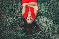 一位身穿红裙的女子躺在绿草地上，笑容满面，享受着阳光明媚的一天