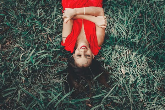 一位身穿红裙的女子躺在绿草地上，笑容满面，享受着阳光明媚的一天