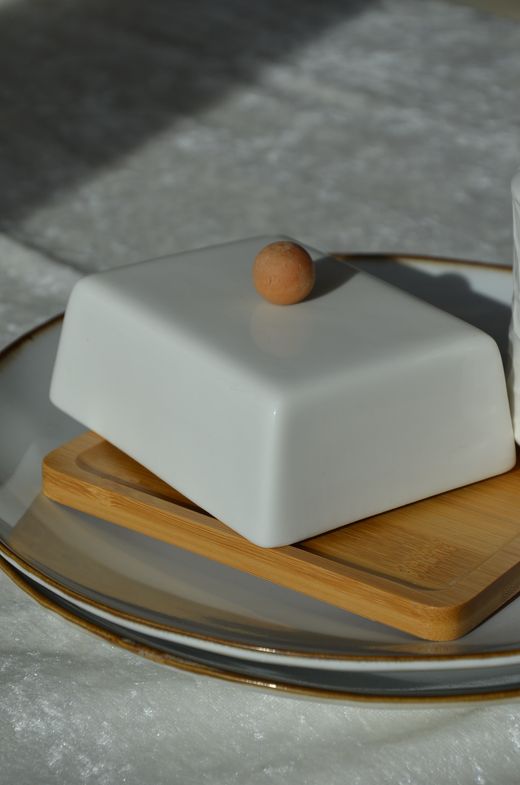 White porcelain butter dish with wooden knob on a bamboo base