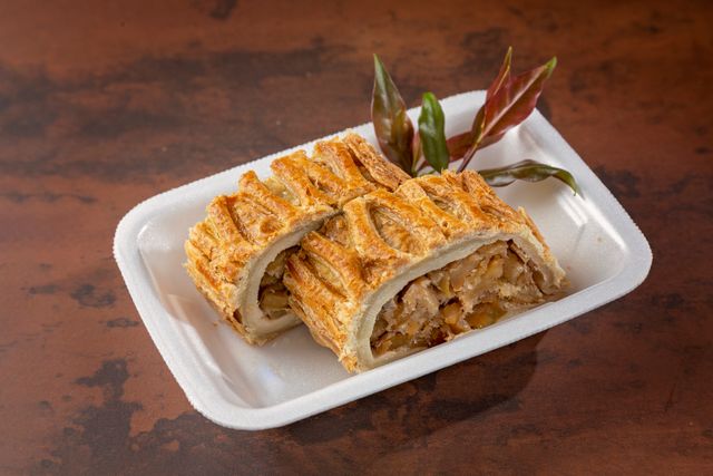 Freshly baked apple strudel on a white plate with decorative leaves, showcasing golden crispiness.