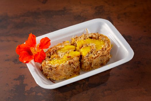 Close-up of a vibrant mango coconut dessert roll with red flower garnish.