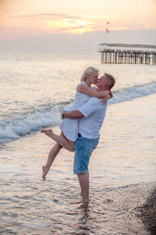 A Man Picking Up a Woman and Kissing on a Beach 