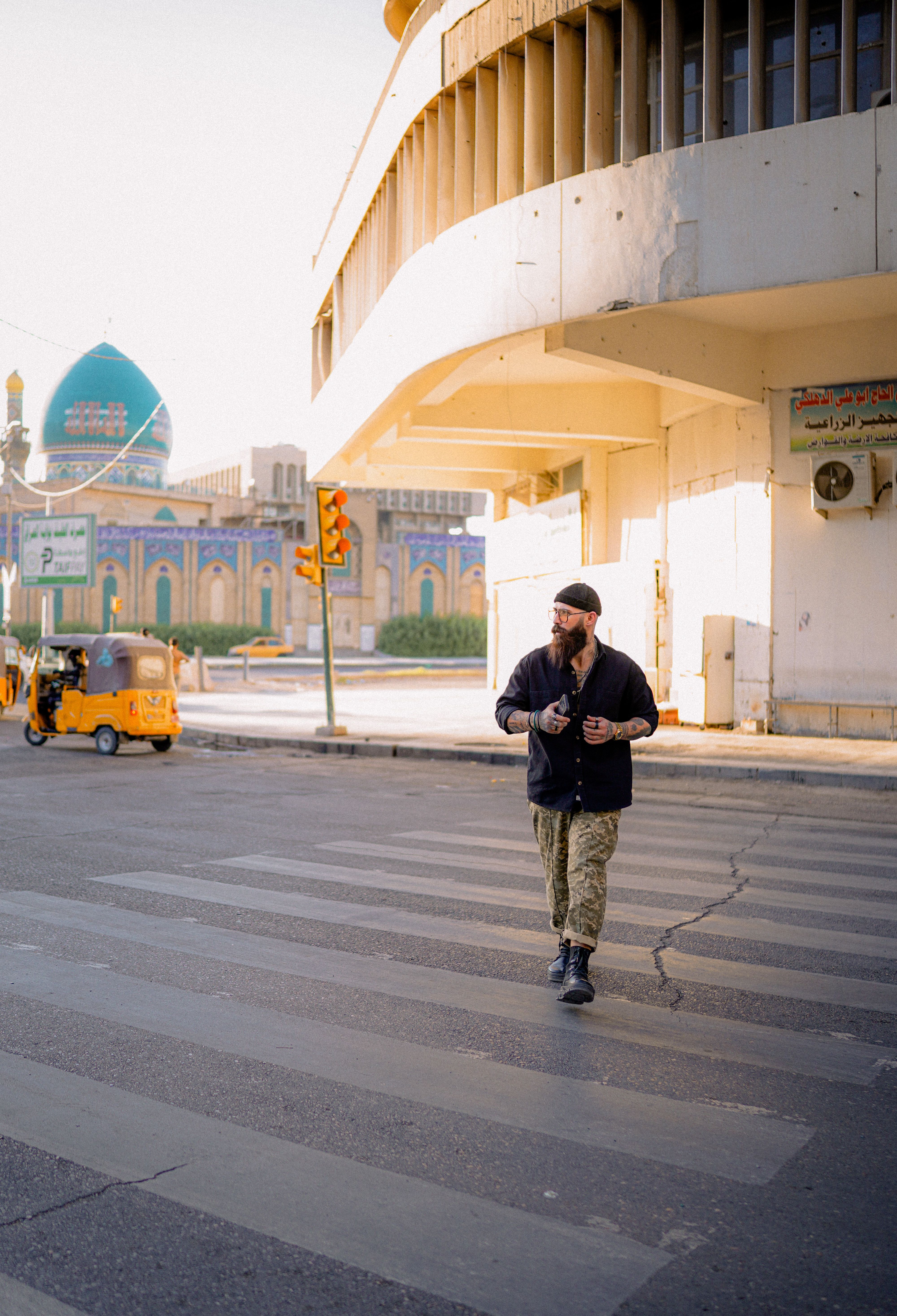 Bearded man in casual attire walking across a city street near architectural landmarks.