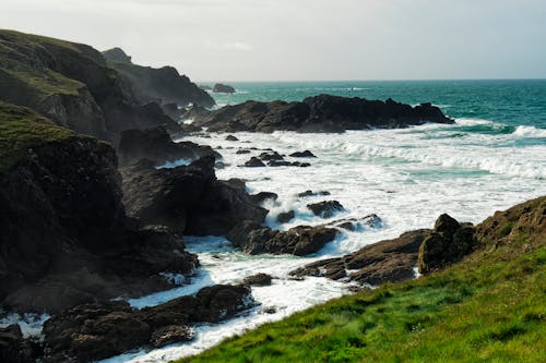 View of Foamy Waves Crashing on a Rocky Shore under Blue Sky 