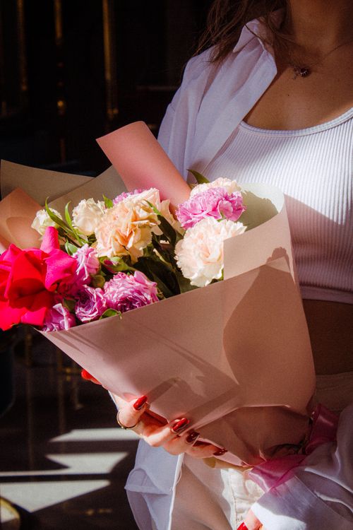 Free A woman holding a vibrant bouquet of flowers with red nails and a white top, captured in natural light. Stock Photo