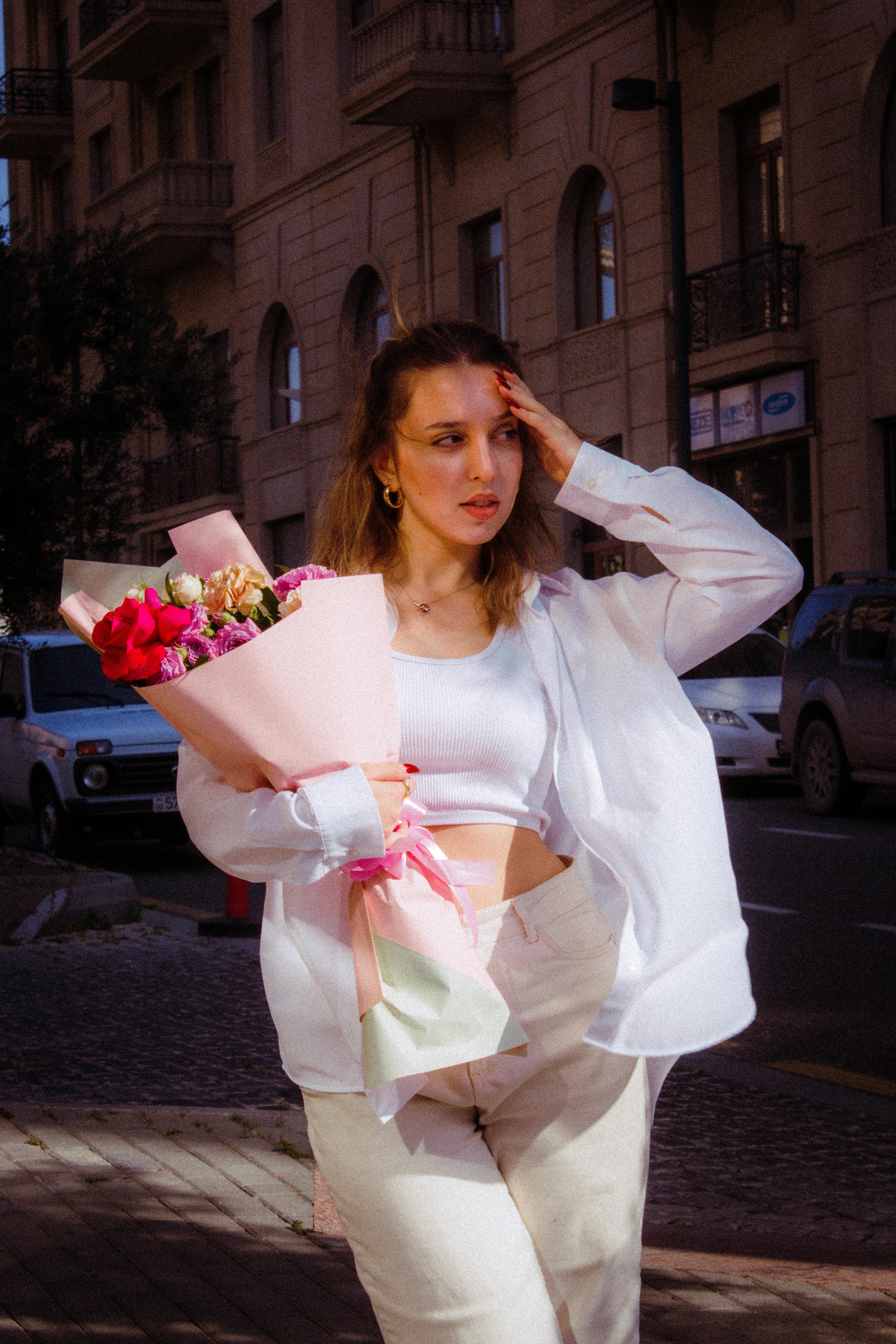 Young woman holding a flower bouquet standing on a city street.