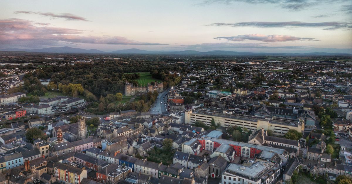 Stunning aerial view of Kilkenny cityscape with Kilkenny Castle at dusk, showcasing residential areas and lush greenery.