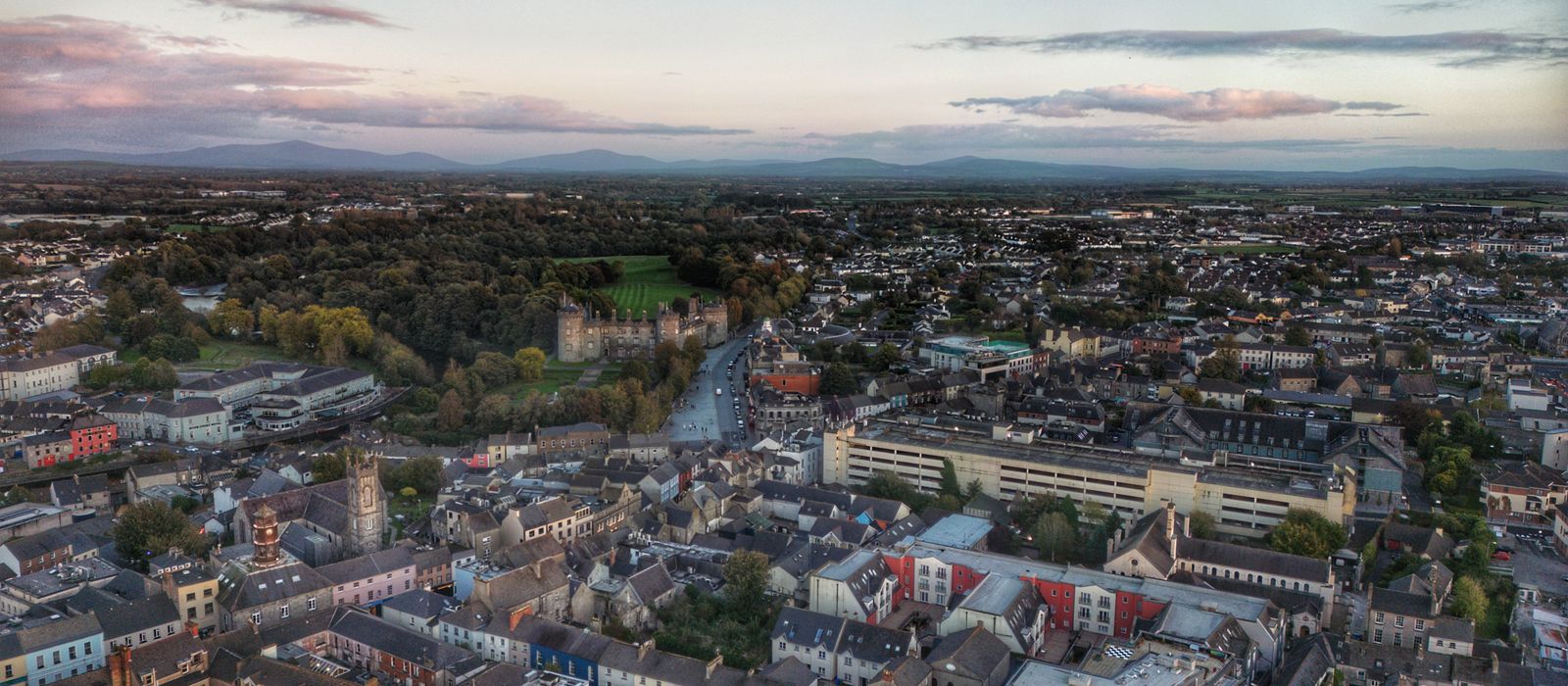 Stunning aerial view of Kilkenny cityscape with Kilkenny Castle at dusk, showcasing residential areas and lush greenery.