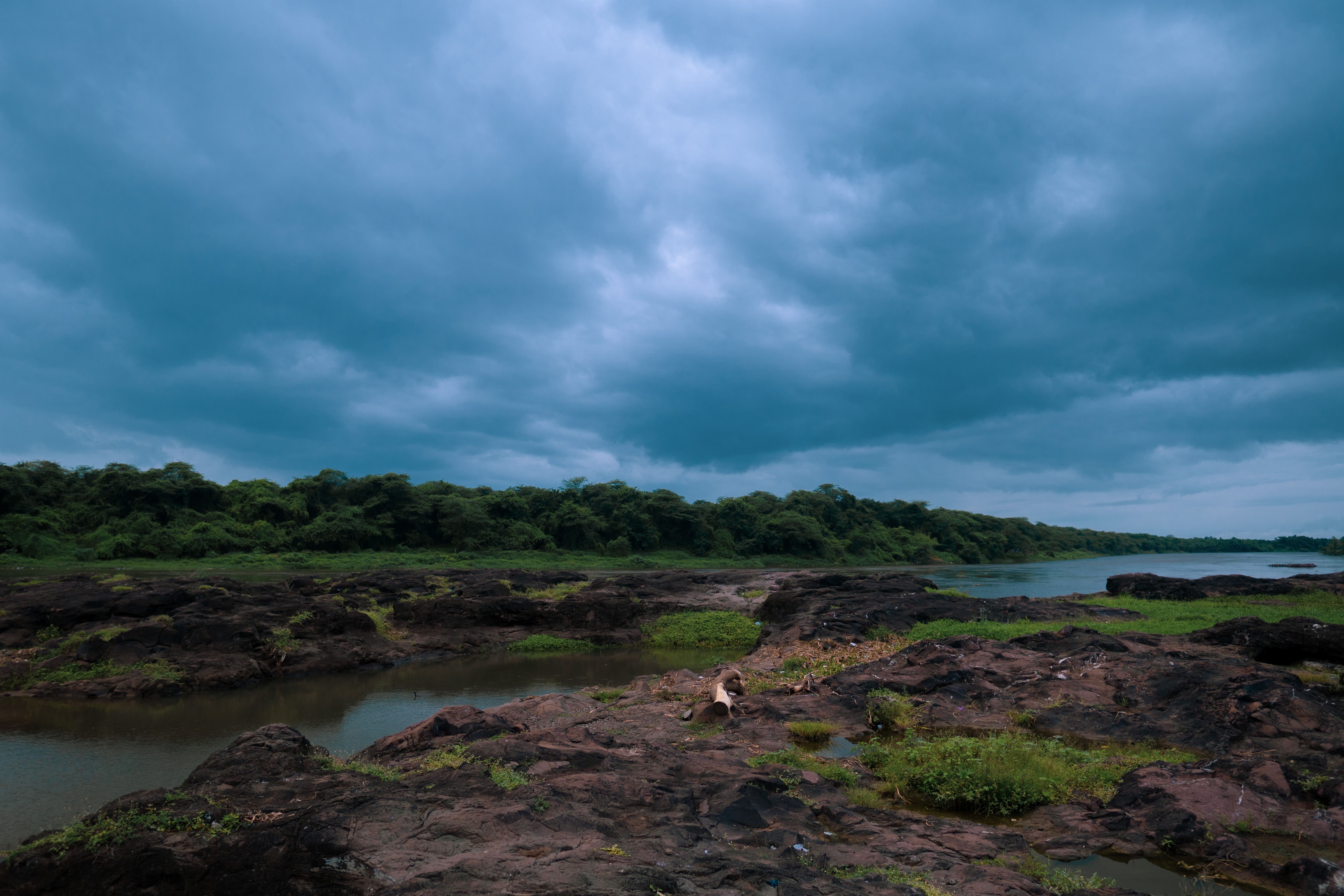 Explore a dramatic cloudy river landscape with lush greenery and rocky shoreline, perfect for nature enthusiasts.