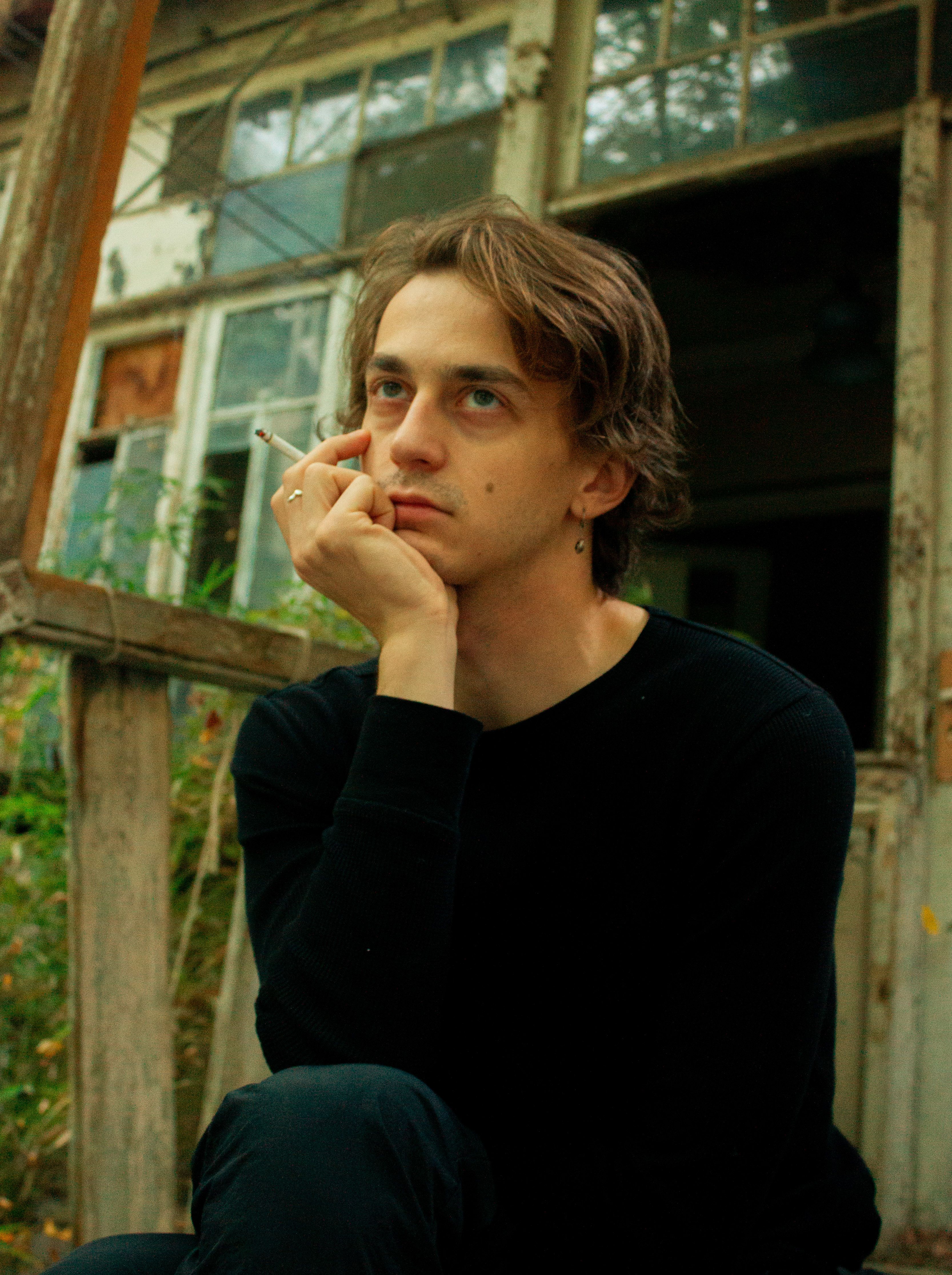A young man in black clothing pondering in front of an abandoned building.