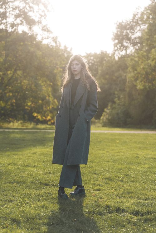 Free Stylish woman in a gray double-breasted coat posing in a sunlit park. Stock Photo