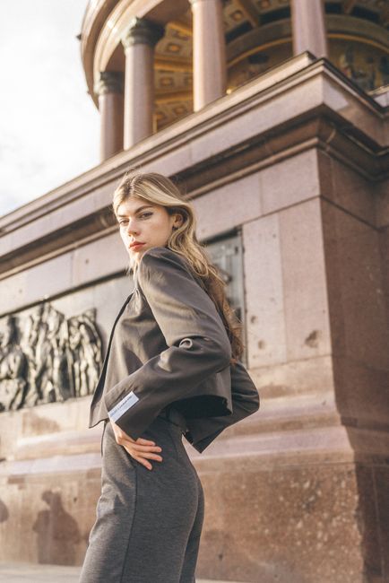 Elegant woman in gray blazer posing confidently by a historic monument in urban setting.