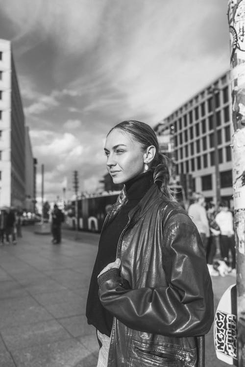 Young Woman in a Leather Jacket Standing on a Sidewalk in City 