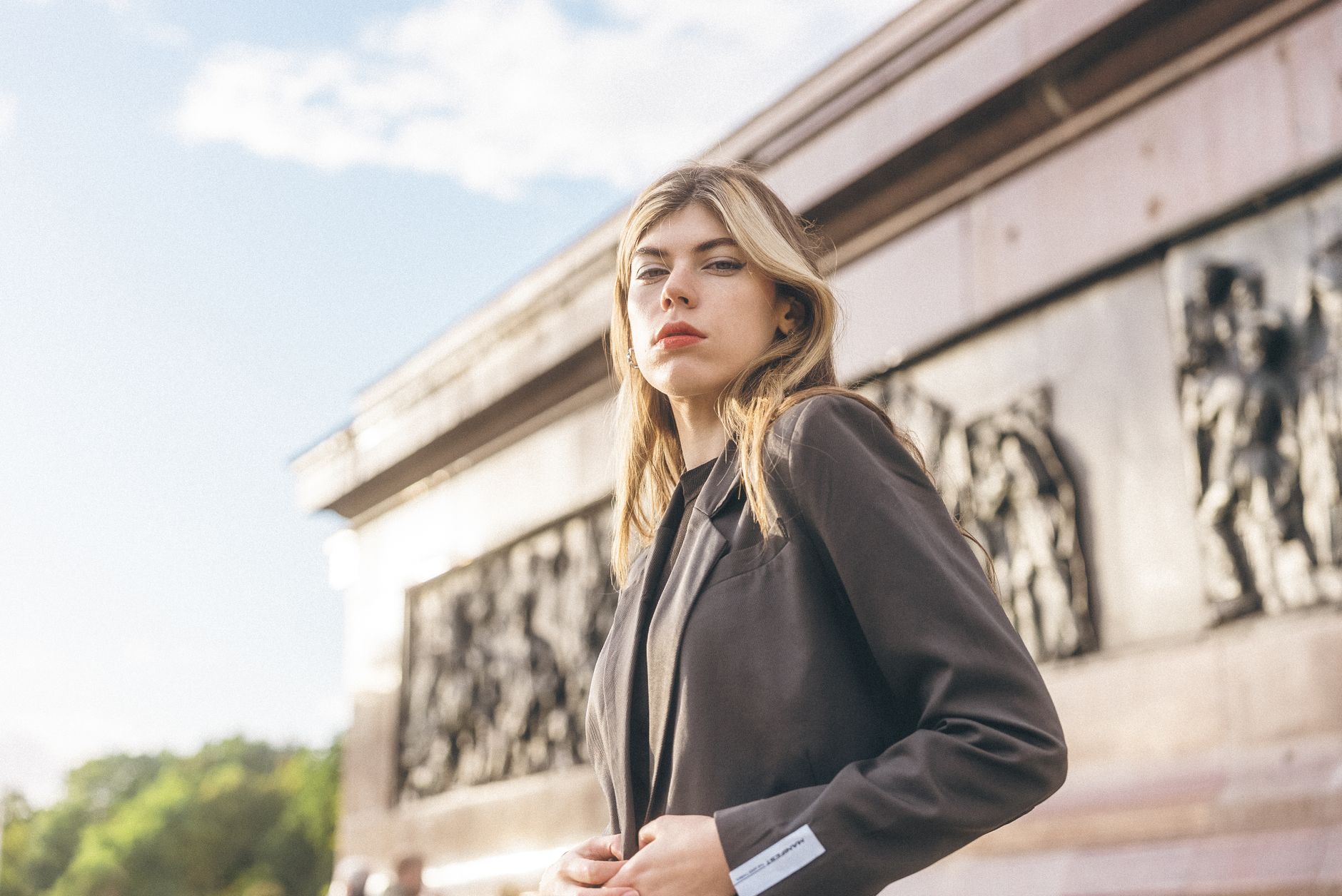 Fashionable woman in a blazer posing outdoors near a historical structure, exuding confidence and elegance.