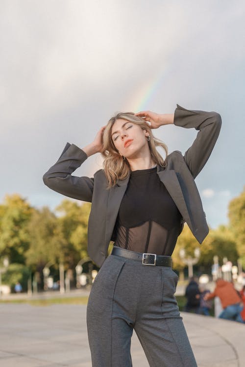 Model in a Gray Blazer and Creased Pants with Raised Arms Posing on the Promenade in the Park