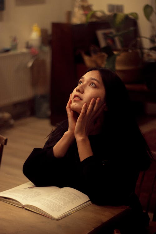 Free Young Woman Sitting at a Table with an Open Book Stock Photo