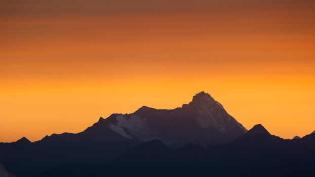 Silhouetted mountain peaks against a vibrant orange sunset sky in the Alps.