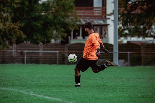 Soccer Player in Orange T-Shirt Kicking a Ball 