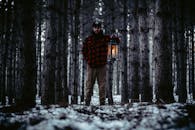 暮色笼罩的雪林中，一个手持灯笼的男人静静伫立，营造出神秘的氛围