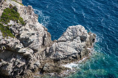Free A stunning view of a rocky cliff meeting the vibrant blue sea on a sunny day. Stock Photo