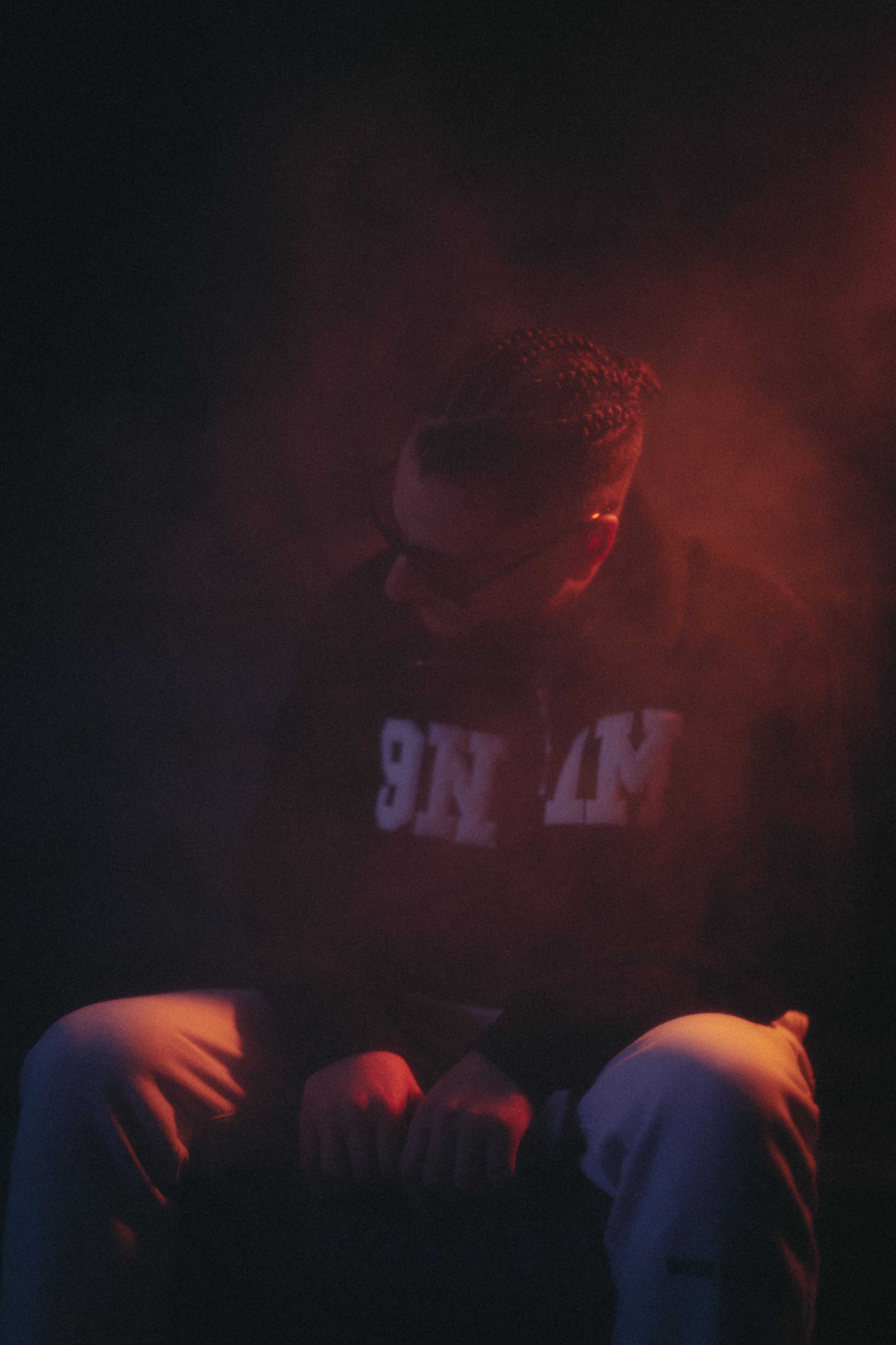 Dramatic portrait of a man sitting in red smoke, wearing a hoodie and sunglasses.