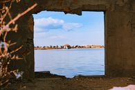 A serene view of a tranquil water scene framed by an abandoned building's window opening.
