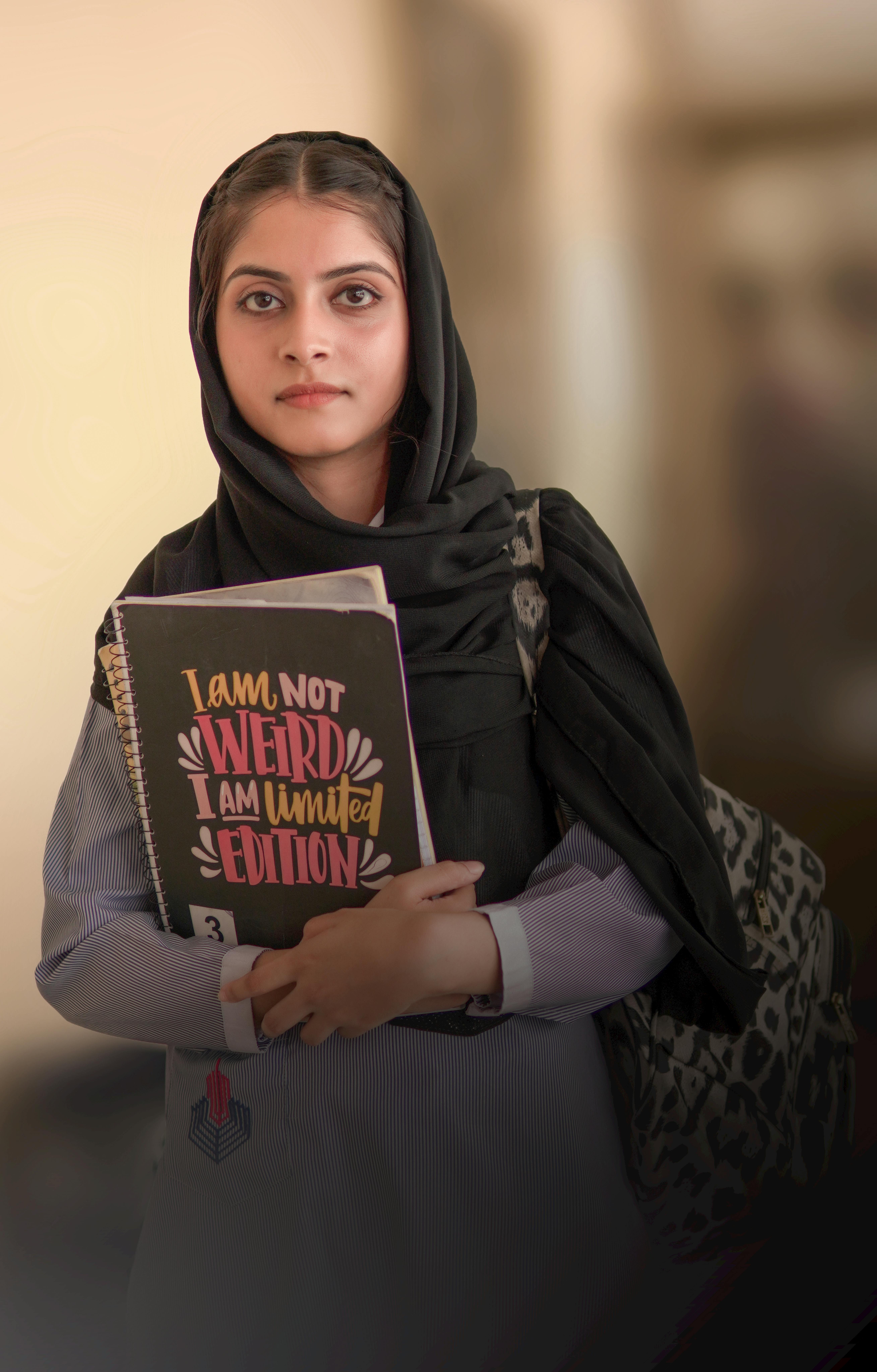 Young woman in hijab holding a notebook in an educational setting.