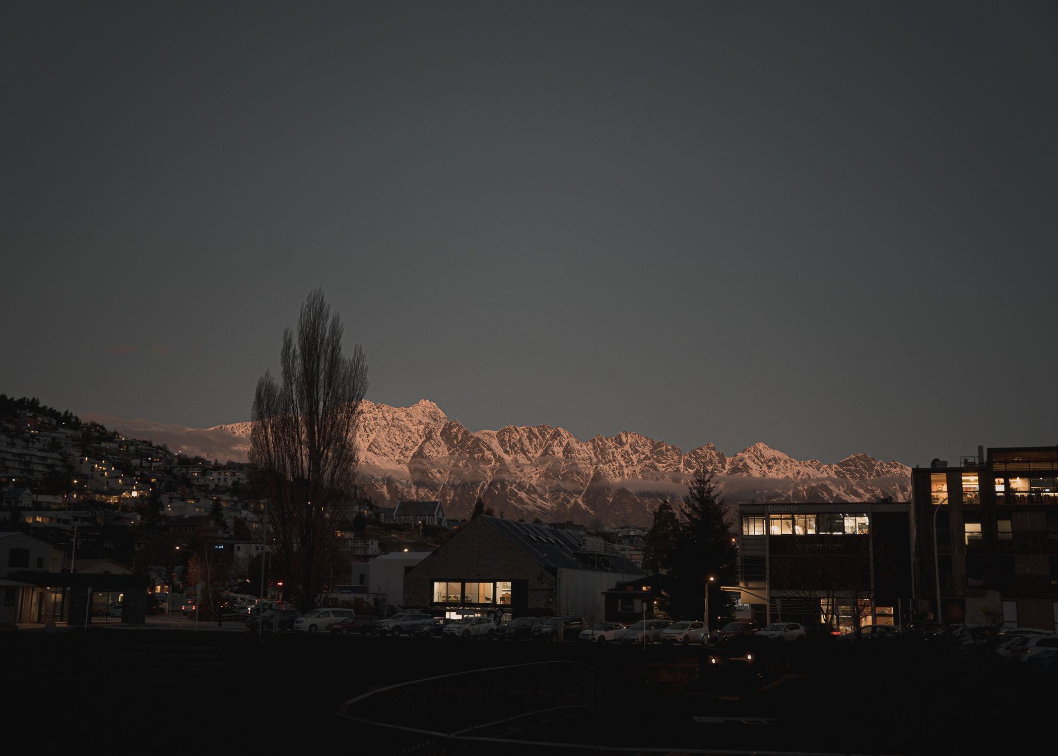 Dusk view of Queenstown, New Zealand with a stunning mountain backdrop and city lights.