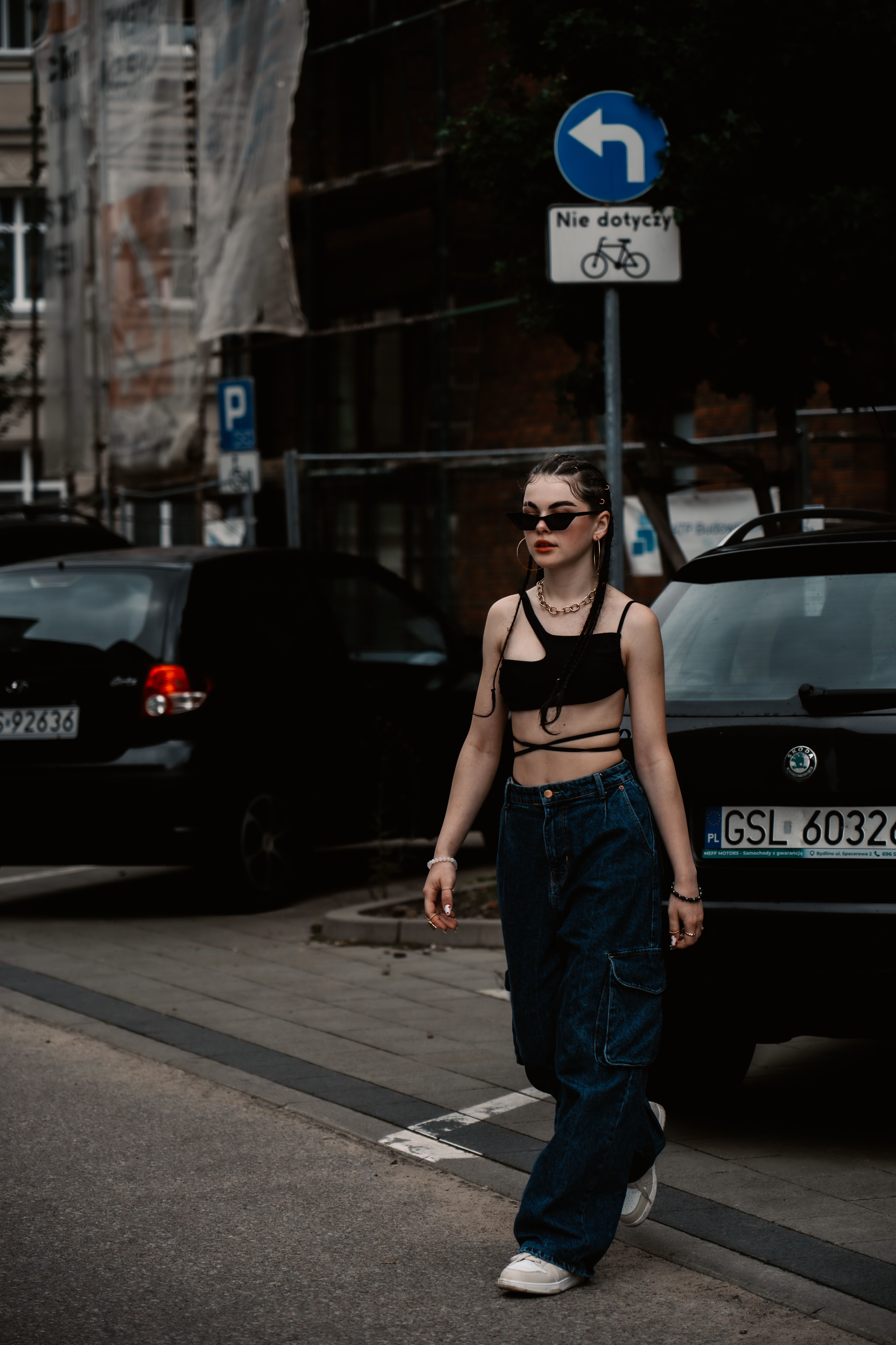 Fashionable young woman in dark attire strolling city sidewalk with cars.