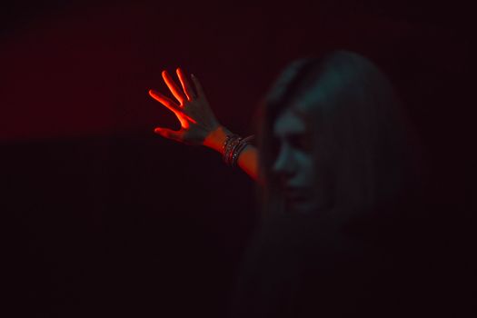 A woman's hand with bracelets reaches into red light, creating a dramatic, artistic scene.