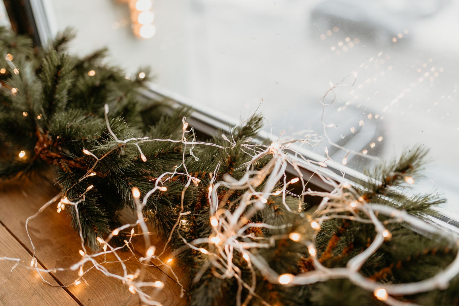 Twinkling string lights wrapped around pine garland on a window ledge.