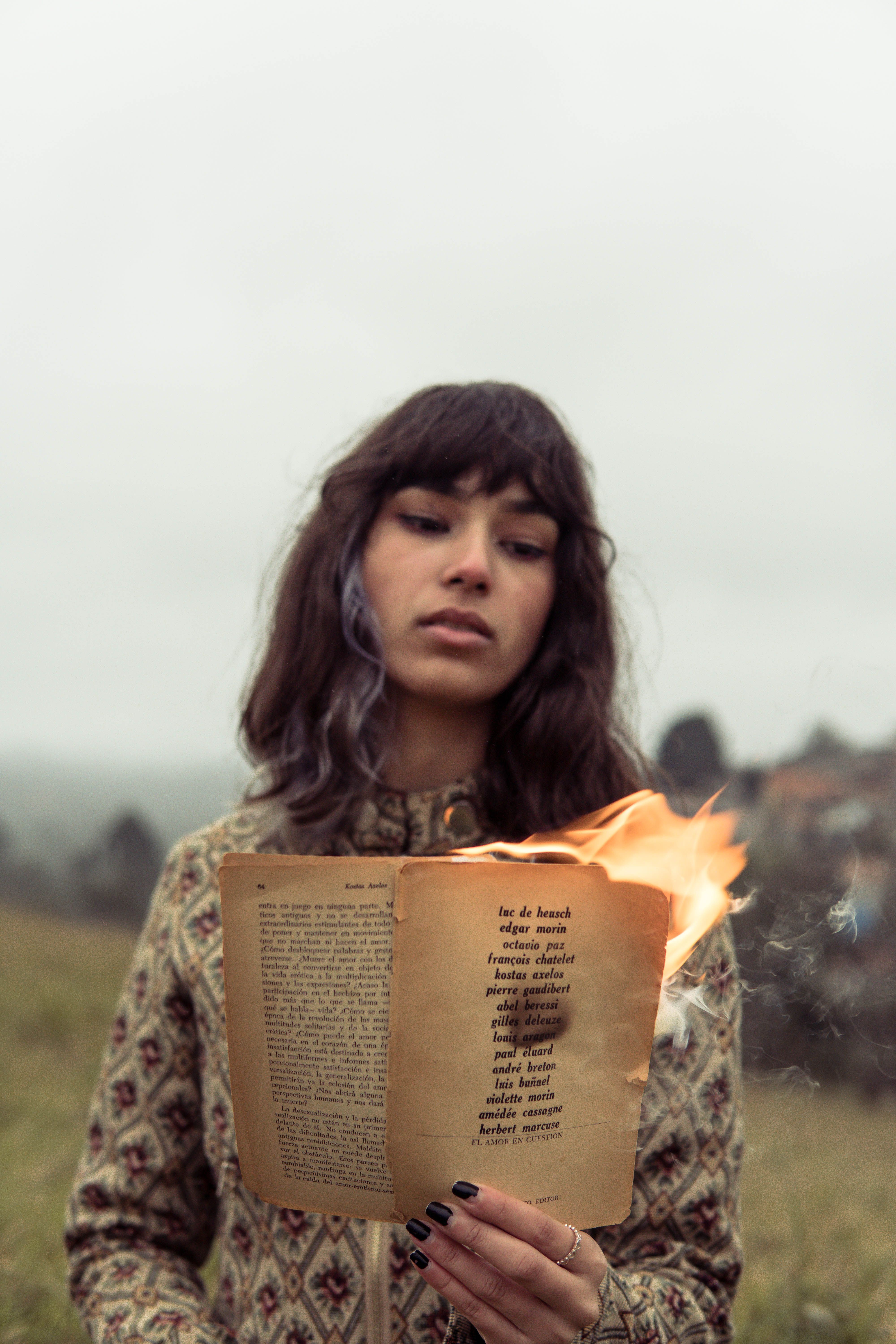 Young woman standing outdoors with a burning book, creating a dramatic scene.
