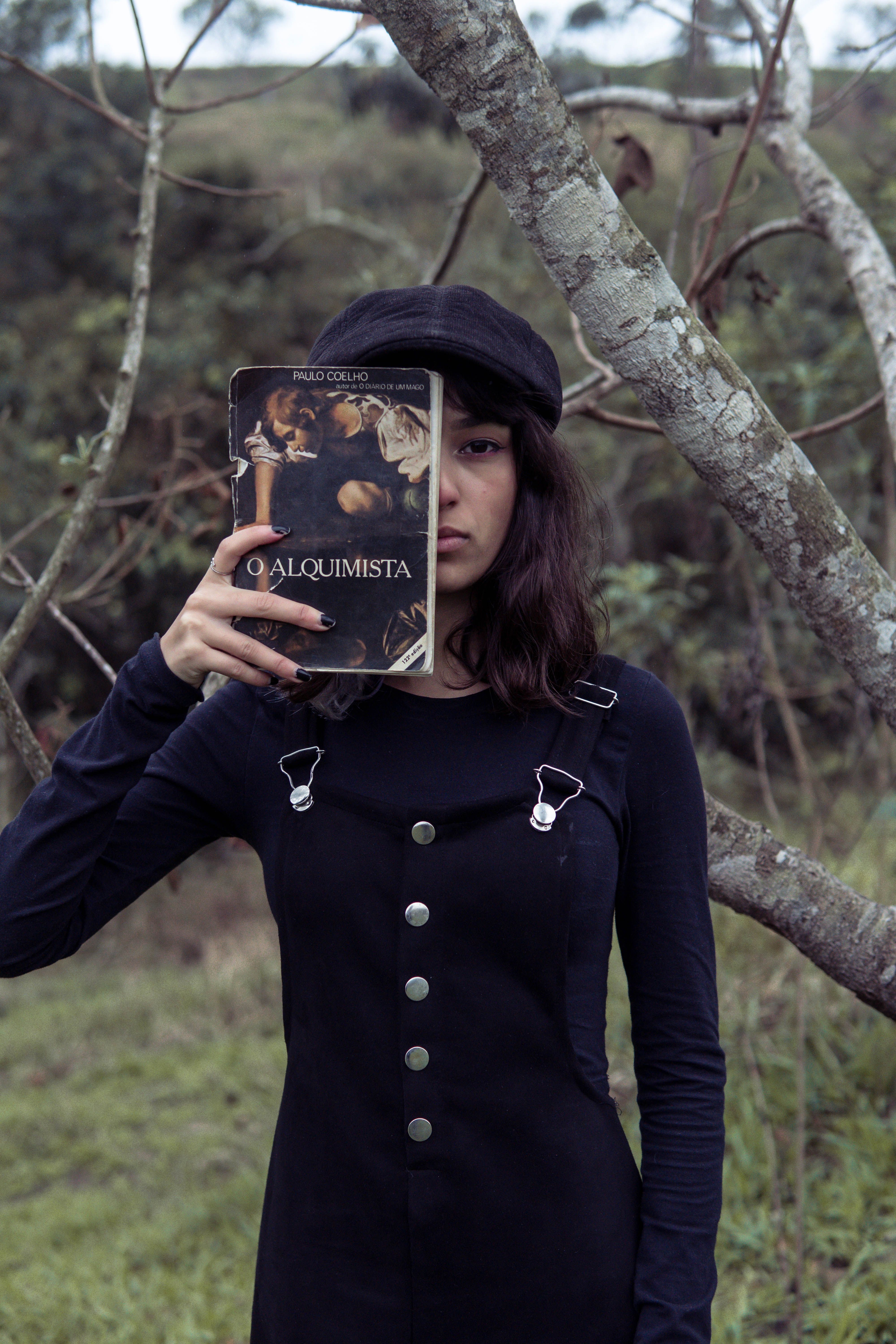 Woman in black dress with a book posing outdoors, capturing a fashion and literary theme.