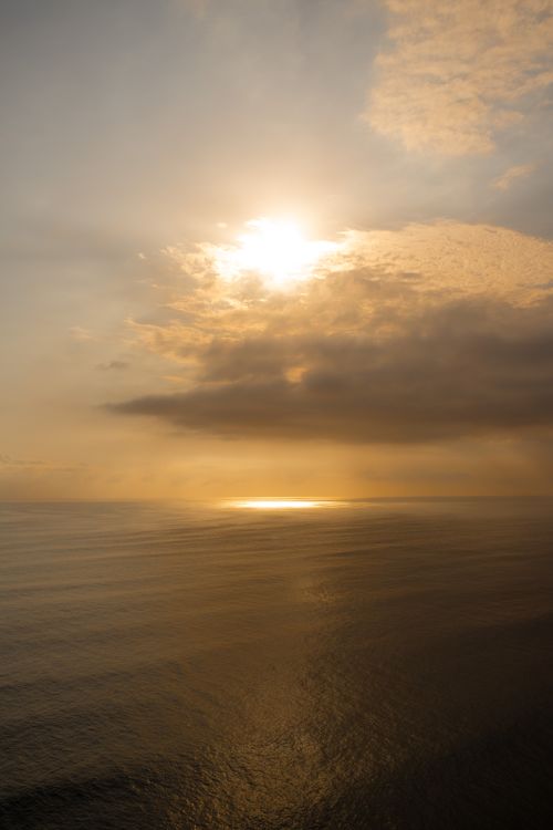 Free Serene view of the sun setting over a tranquil ocean with warm golden reflections. Stock Photo