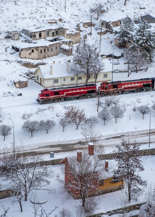 Birds Eye View of a Red Train Riding through a Village in Winter 