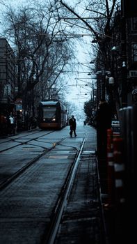 Couple walking near tram on misty evening street in İstanbul, capturing urban vibe.