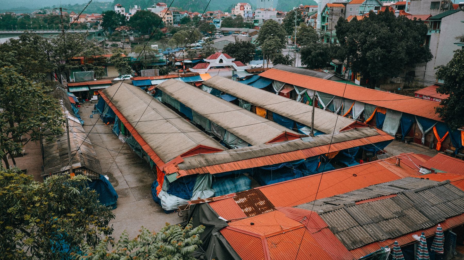 Luftaufnahme des lebhaften Stadtmarktes in Lạng Sơn, Vietnam, umgeben von üppigen Bäumen und städtischen Gebäuden.