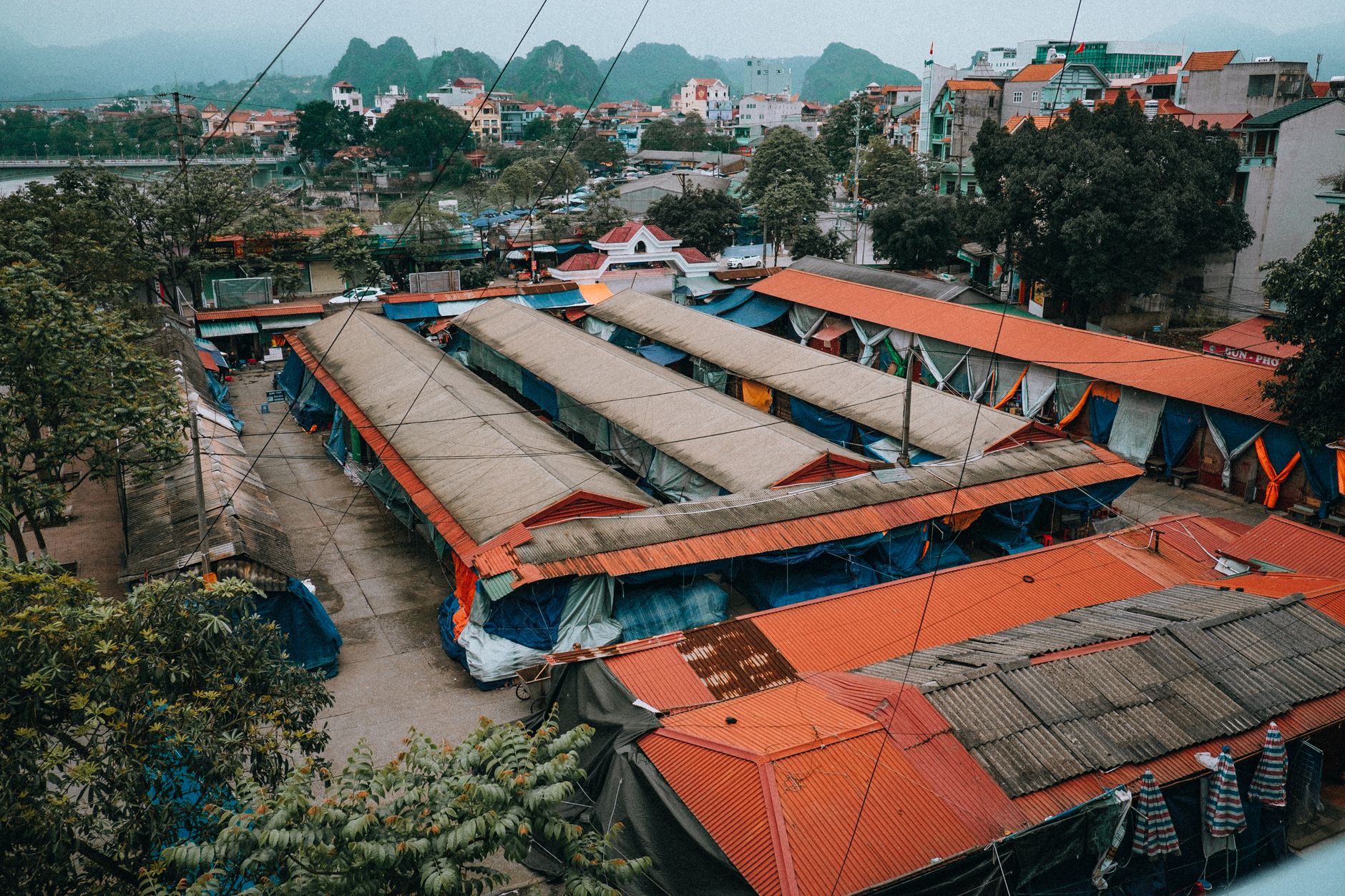Aerial shot of the vibrant city market in Lạng Sơn, Vietnam, surrounded by lush trees and urban buildings.