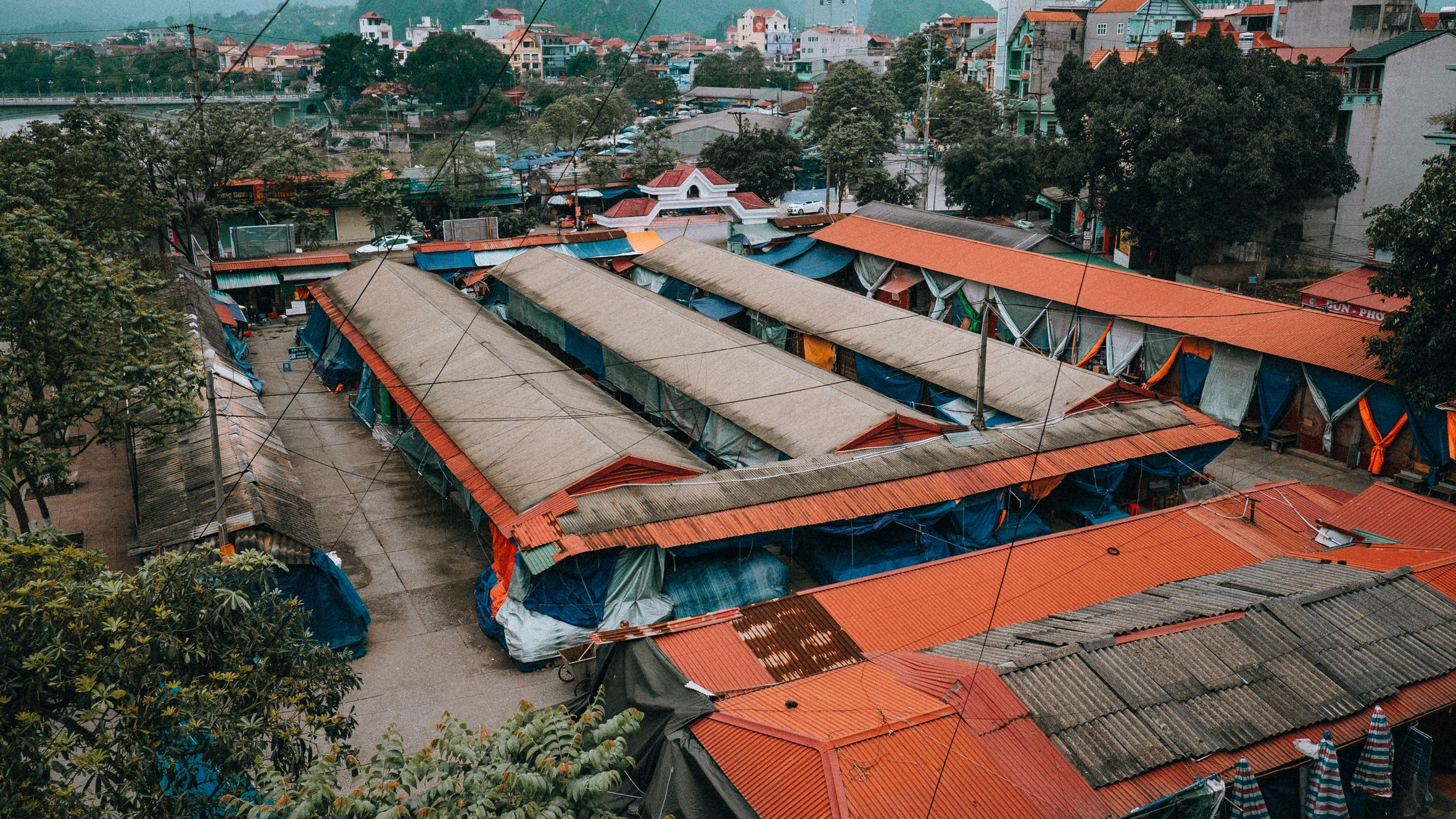 Aerial shot of the vibrant city market in Lạng Sơn, Vietnam, surrounded by lush trees and urban buildings.