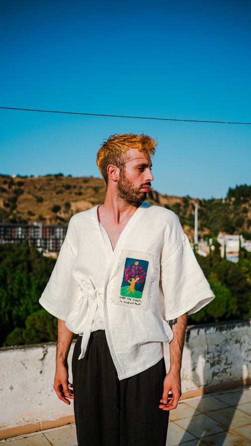 Free A young male model in a stylish outfit posing outdoors under a clear blue sky. Stock Photo