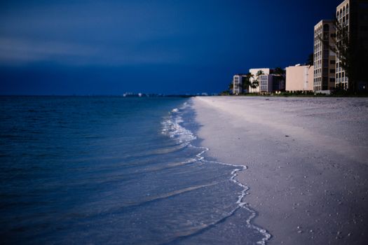 Discover serenity with ocean waves gently lapping at a pristine beach near coastal buildings, during twilight.