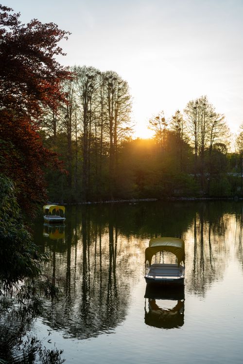 Free Serene sunset over a calm lake with rowboats reflecting on the water. Stock Photo