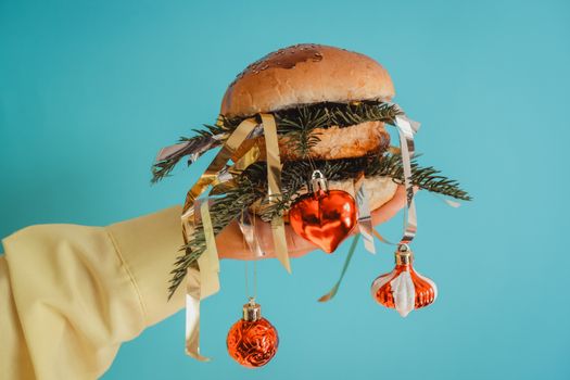 Creative burger with Christmas decorations and ornaments on a bright blue background.