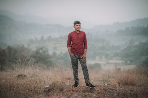 Free A young man in casual attire stands on a scenic hillside with a misty autumn backdrop. Stock Photo