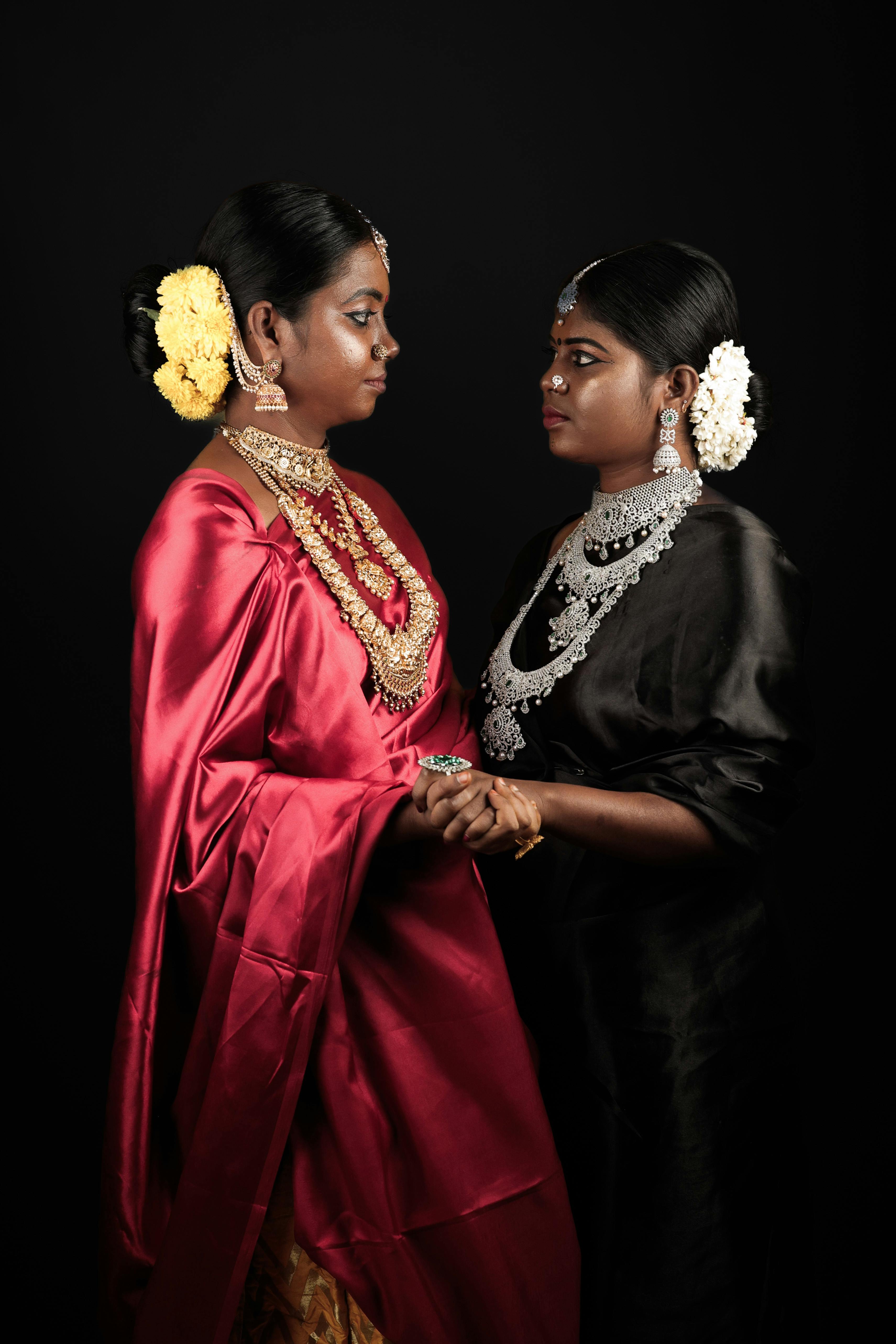 women in satin saris and traditional indian jewelry looking into each other eyes