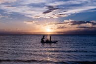 在宁静的海洋背景下，日落时显现出船和渔夫的轮廓