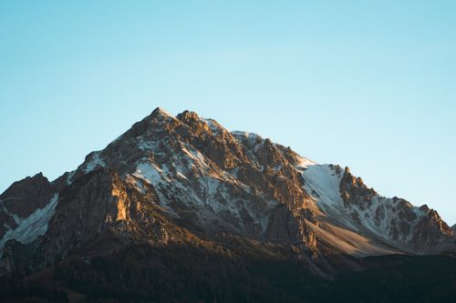 Free A stunning view of a rugged snowcapped mountain under a clear blue sky during sunrise. Stock Photo